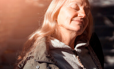 An elderly smiley wooman feels happy, walks in a park outdoors in the rays of a sun.