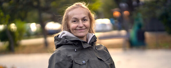 Old cheerful woman with a smiiley face walks in the city in the autumn sunny day.