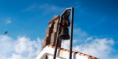 A small chapel with a bell tower, a Christian church against a bright sky background with flying birds.