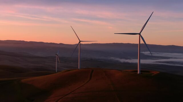 Wind turbines stand tall on rolling hills at sunset, generating clean energy in Altamont Pass, Livermore, California, USA. The scene showcases sustainable power production.