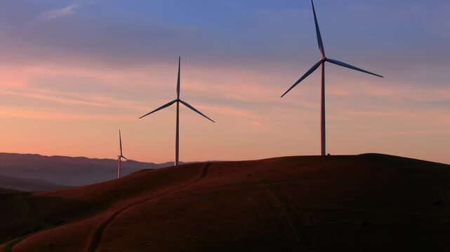 Wind turbines stand tall on rolling hills at sunset, generating clean energy in Altamont Pass, Livermore, California, USA. The scene showcases sustainable power production.