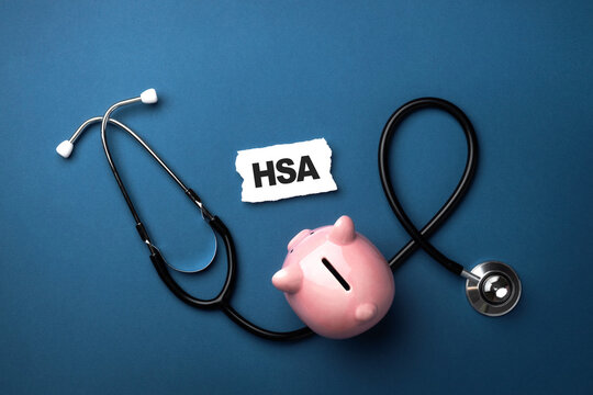 Stethoscope wrapped around pink piggy bank with "HSA" written on piece of paper on blue background symbolizing health savings accounts. Top view, flat lay. - Powered by Adobe