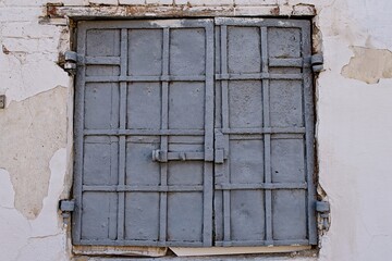 Vintage blue metal window shutters on a vibrant gray textured wall, with graffiti at the bottom.