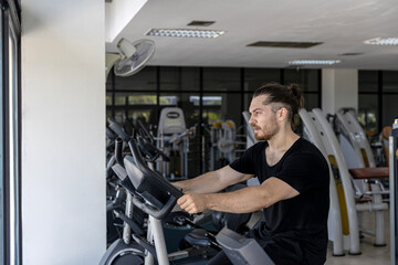 Attractive good looking fitness trainer shows how to use Elliptical Trainer to improve leg strength and building muscles in a gym. A sport man is running on a Elliptical Trainer to start his workout