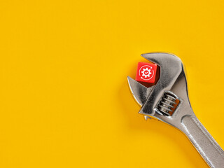 Adjustable wrench holding red cube with efficiency optimization symbol on yellow background