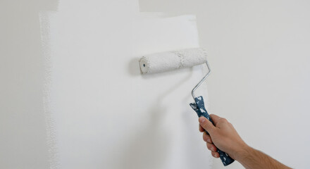 Male hand painting wall with white paint roller. Painting apartment, renovating concept