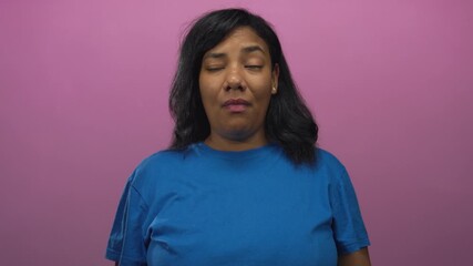 African american woman grimaces in studio with purple backdrop wearing blue shirt and loose hair under soft lighting; disgust.