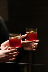 Hand Holding Red Cocktail with Citrus Peel and Ice Cube in front Mirror