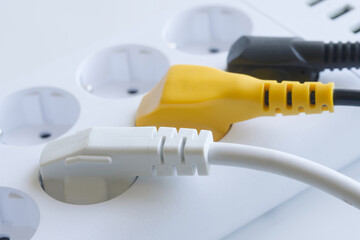 Close-up of a white power strip with three colorful European plugs inserted, highlighting modern...
