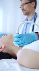 Doctor man wearing blue protective gloves is using ultrasound machine to examine neck of female...