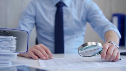 Businessman is carefully examining financial documents with a magnifying glass, highlighting the...