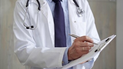 Male doctor filling medical form on clipboard, writing prescription, making notes. Medicine and...