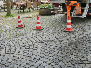 Man in an orange jumpsuit is working on a sidewalk with three red