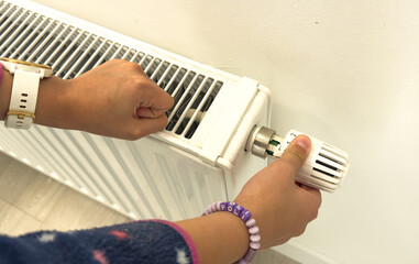 The child's hands warm their hands near the heating radiator. Saving gas in the heating season.