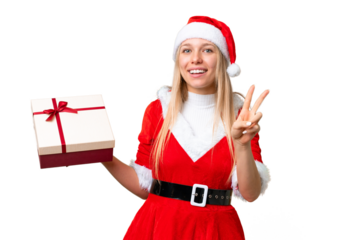 Young blonde woman with christmas hat and holding a gift over isolated chroma key background smiling and showing victory sign