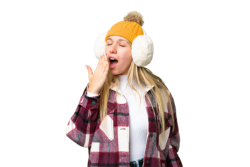 Young pretty blonde woman wearing winter muffs over isolated chroma key background yawning and covering wide open mouth with hand