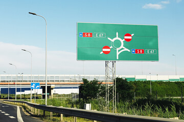 Highway road sign with roundabout scheme. Green direction board near exit. No entry red symbols....