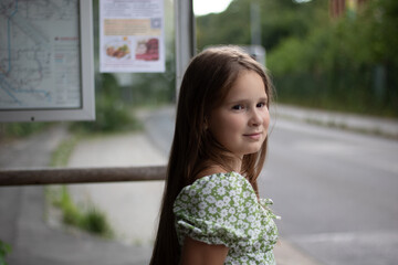Fototapeta premium Young Girl Waiting at Bus Stop in Floral Dress