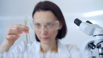 Scientist researcher with protective glasses examining lab tube with a green fluid. Microbiology...