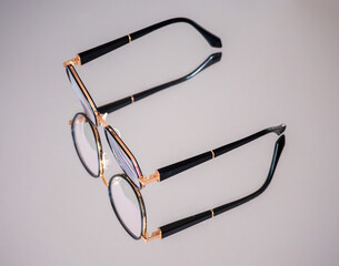 Modern round eyeglasses with black temples and gold frame placed on light reflective surface,...