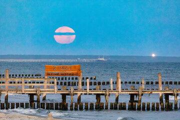 Vollmond &uuml;ber dem Fischersteg in Zingst an der Ostsee, im Hintergrund Prerower Seebr&uuml;cke und Leuchtfeuer Dar&szlig;er Ort.