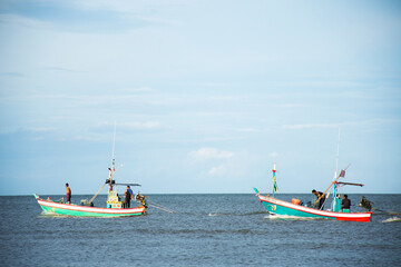 Fototapeta premium Thai fisher man sailing wooden fishing boat to trawl laying fish net or wood fishery ship trawling net catch fish marine life at Phetburi Beach in sea ocean on June 28, 2025 in Phetchaburi, Thailand