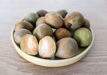 Fototapeta premium Manilkara zapota or Sawo Fruit or commonly known as Sapodilla, Sapota, Chikoo, Chico, Naseberry, or Nispero. Half Buah SAwo on a flat Plate Above Wooden Table