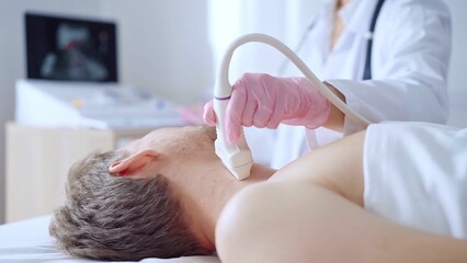 Doctor woman with pink medical gloves performing neck ultrasound exam on male patient. Thyroid...