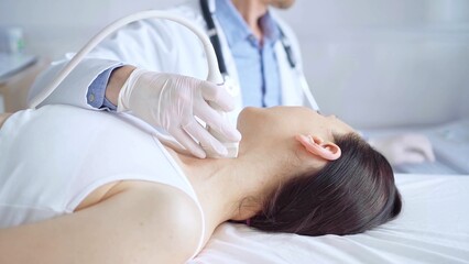 Doctor man is using ultrasound equipment on neck of female patient lying down for a medical...