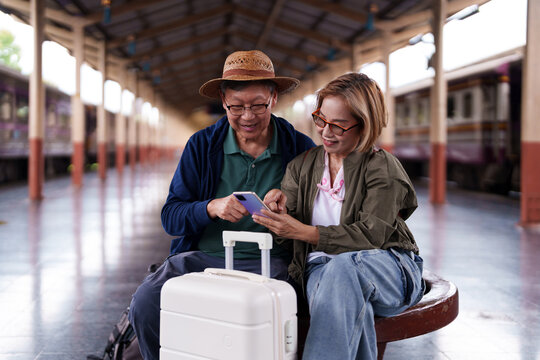 Asian Senior Couple Travelers Happy Using Mobile Phone at Train Station Platform Trip Planning Destination Search Online Booking App - Powered by Adobe