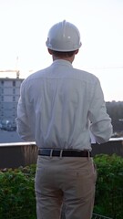 Male constructive engineer wearing white shirt and hard hat is writing on a clipboard while...