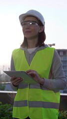 Woman a construction engineer with a white hard hat and safety vest is using digital tablet while...