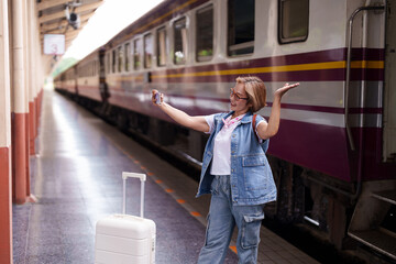 Asian senior woman tourist traveler taking selfie smartphone enjoying modern rail travel adventure journey train station platform happy smile