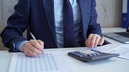Businessman accountant with blue suit is calculating numbers for a financial audit and taking notes...