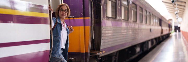 Older Asian woman traveler at train station platform ready for her journey embracing the adventure...