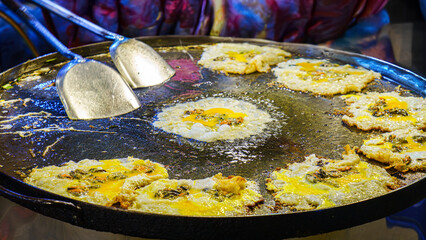 Close-up of traditional Thai oyster omelet frying on a giant pan, highlighting street food culture,...