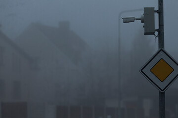 A traffic light is visibly hanging from a pole amidst the thick fog that permeates the atmosphere,...