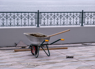 An iron wheelbarrow with dirt and a shovel on the street.