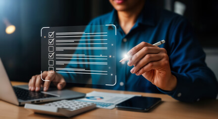 A businessman uses a stylus to check off items on a digital checklist displayed on a futuristic interface, while working on a laptop in a modern office setting