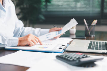 Office businesswoman hand to operate calculator analyzing financial data, counting costs on desk. accounting, financial analysis for business budget planning, calculation support, finance management.