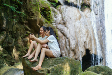 Asian Indonesian Women Using Smartphone by Waterfall During Nature Travel in Yogyakarta
