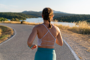 Young woman jogging on country road near lake in summer