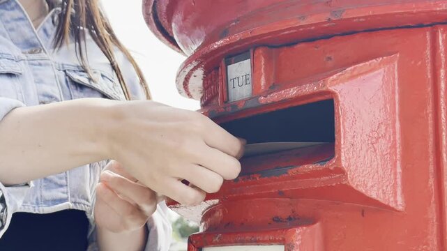 Young lady near a red mailbox sending paper letters in quiet vintage street
