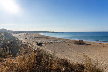 View of Praia da Rocha beach in Portimão, Algarve, Portugal. Golden sand, dramatic cliffs and blue Atlantic ocean under a clear summer sky.