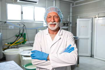 Portrait of senior food technologist in sterile clothing standing in dairy production factory controlling quality.