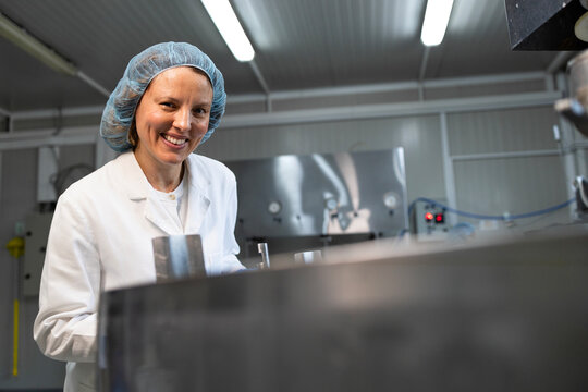 Portrait of female food technologist in sterile clothing standing in dairy production factory controlling quality.