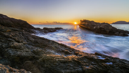 Obraz premium Fiery Sunset Over a Rocky Shoreline