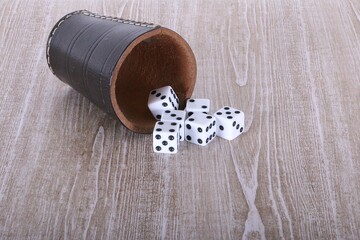 close-up of a leather dice cup lying on a wooden table with white dice