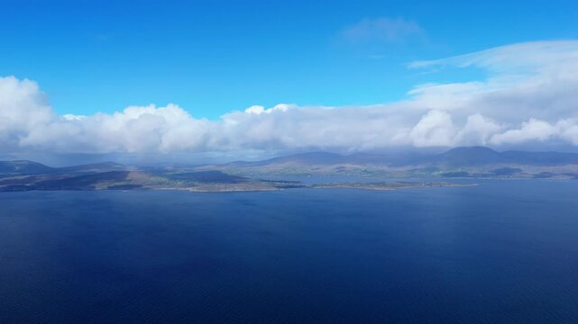 Seascape showing the coastline and mountains of County Kerry in Ireland. The Dingle Peninsula is partially obscured by clouds on a beautiful day.