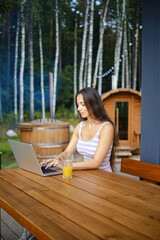 A woman finishes remote work while sitting on the terrace and is about to go to outdoor sauna